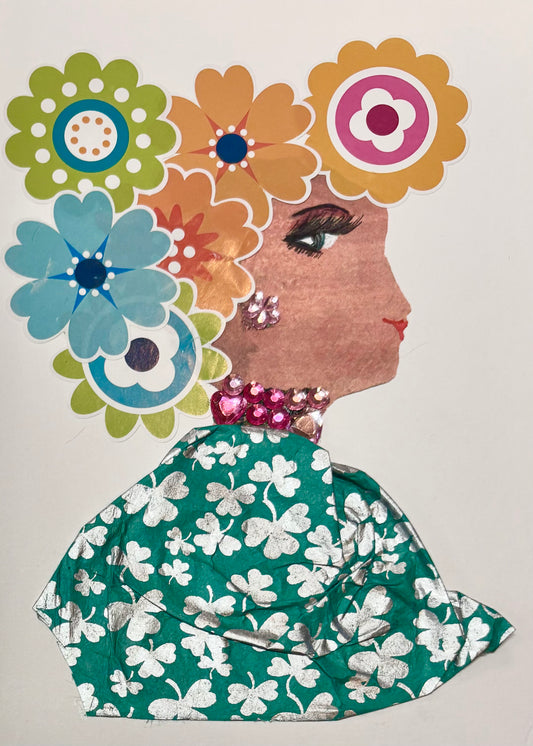 This is a handmade card of a woman named Lady Aldgate. Her hair is made from a colourful arrangement of large paper flowers in orange, blue, green, yellow, and pink. She wears sparkly pink gem earrings and a matching necklace. Her outfit is created from green fabric with a bold silver clover pattern.