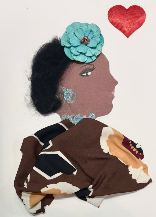 This is a handmade card of a woman named Kensington Katelyn. Her hair is made from soft, dark fibres and decorated with a large teal flower. She wears glittery blue earrings and a matching necklace. Her outfit is made from patterned brown fabric with cream, black, and mustard floral shapes. Her face is shown in profile with gentle features and pink lips. A red heart embellishment floats above her head.