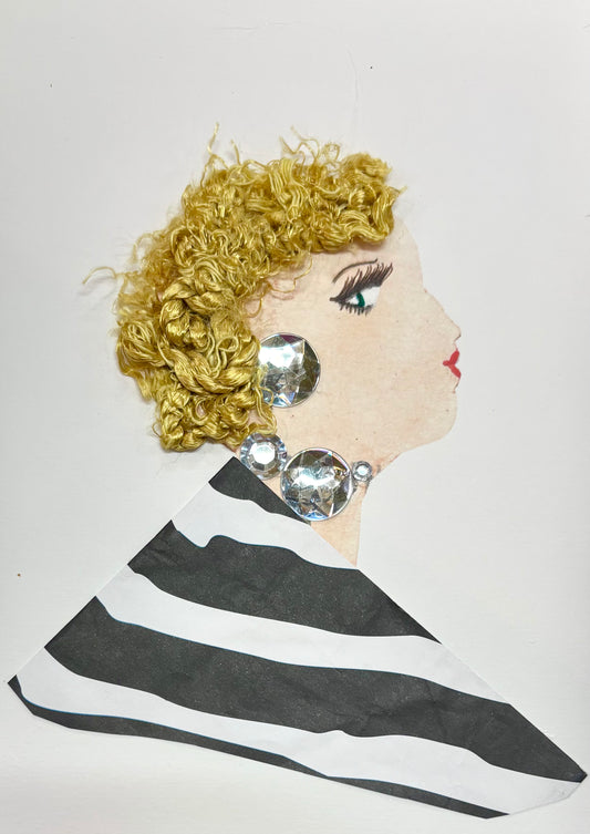 I handmade this card of a woman named Kingsbury Kira. She’s shown in profile with curly golden yarn hair, red lips, and dramatic lashes. Her jewellery sparkles with oversized clear gems along her ear and neckline. She wears a bold black-and-white striped outfit that adds to her striking, modern style.