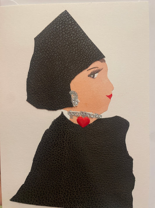A handmade card of a woman in profile wearing a black textured outfit and headpiece. She has a silver gem earring and a sparkly necklace with a small red heart at the centre.