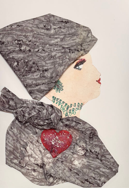 This is a handmade card of a woman named Millie Marylebone. She wears a textured grey headwrap and matching garment, both made from soft, marbled fabric. A sparkling red heart is placed on her chest. Her jewelry is drawn in a teal color with loops around her neck and a floral earring. Her expression is calm, with red lips and long lashes.