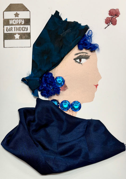 A woman has a deep blue headwrap with her curly blue hair peaking out. She has a dark blue blouse and wears blue gem earrings and a necklace. There is a "Happy Birthday" sticker in the top left and a dainty flower in the top right. 