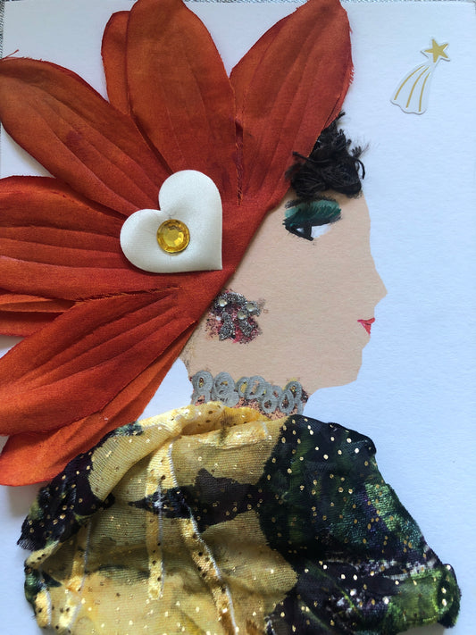 This is a handmade card of a woman named Orange Flower. She wears a dramatic headdress made of large orange petals, decorated with a white heart and a yellow gem. Her earring and necklace sparkle with glitter and painted detail. She is dressed in soft yellow and black sheer fabric with gold specks. Her face is drawn in profile with green eye makeup, red lips, and carefully styled hair. A small shooting star sticker appears in the top corner.
