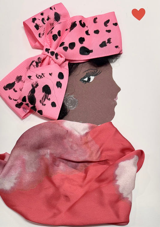 A woman wears a large pink bow with black polkadots on her head. Her blouse is a coral pink with some white accents. There is a small red heart in the top right corner. 