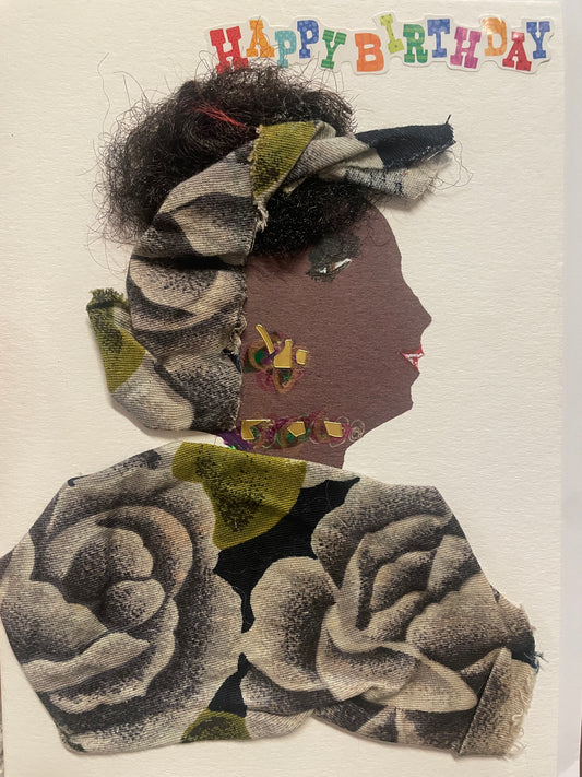 This is a handmade card of a woman named Temi Tope. Her hair is styled with black textured fibres and wrapped in floral fabric that matches her outfit. She wears a necklace and earring made of multicoloured gems. Her outfit is crafted from fabric featuring large grey roses with touches of green. At the top, colourful letters spell out “Happy Birthday.”
