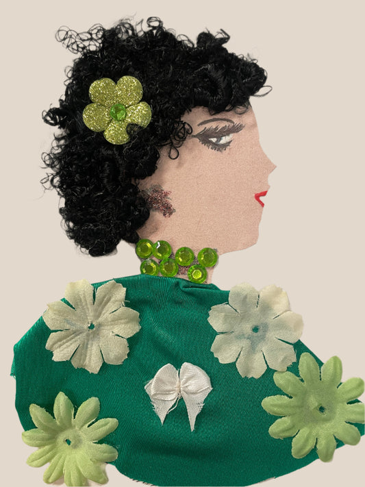 This is a handmade card of a woman named Zariah Greenleaf with curly black hair, a sparkly green flower, and a green dress decorated with soft fabric flowers and a white bow.