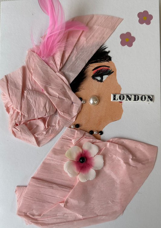 This handmade card that I created is over London Lily. She is dressed in a light pink blouse and hair piece. Her blouse has a cherry blossom attached, and a pink feather in her hair. She has pearl like earrings and London written across her mouth. There are also more flowers on the card. 