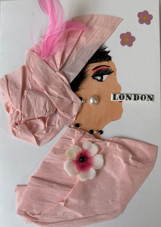 This handmade card that I created is over London Lily. She is dressed in a light pink blouse and hair piece. Her blouse has a cherry blossom attached, and a pink feather in her hair. She has pearl like earrings and London written across her mouth. There are also more flowers on the card.