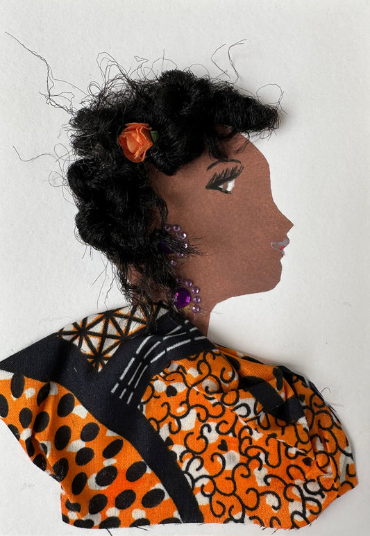 This handmade card of Islington Illianna is of a woman dressed in an orange and black Ankara. Her hair has an orange flower clip, and she is wearing purple gemstone jewellery.