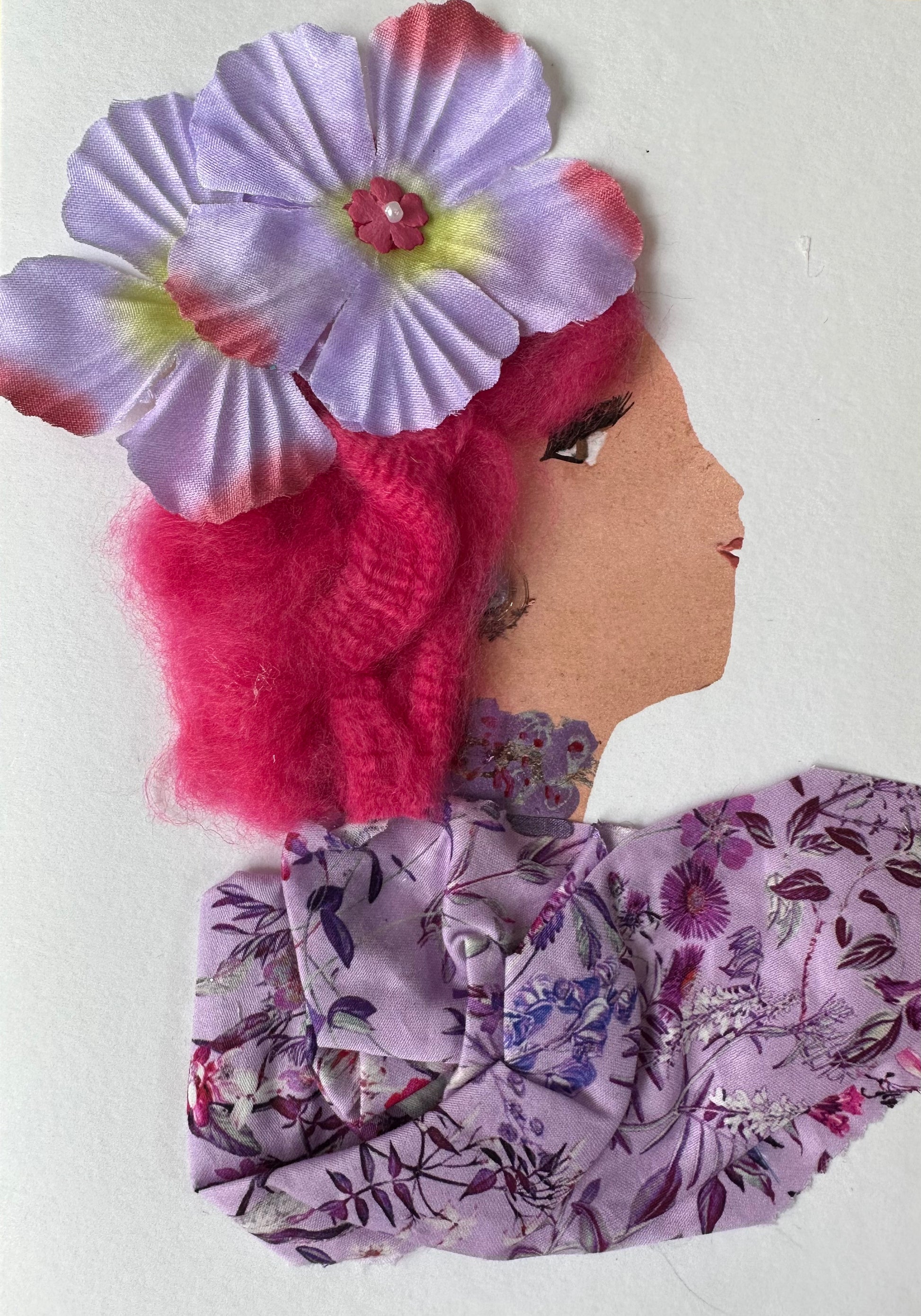 This handmade card is of a woman dressed in a purple, floral patterned blouse. Her electric pink hair has two light purple flowers attached.