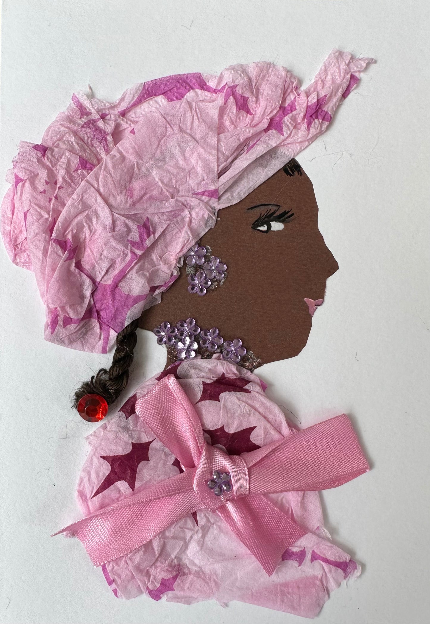 I designed this handmade card of a woman named Euston Evelyn. She is dressed in a pink blouse and hatinator. The blouse is tied together with a pink ribbon and has a light purple flower gemstone in the center. Her jewellery is also made up of the same light purple gemstones, and her hair is pinned together with a ruby red gemstone.