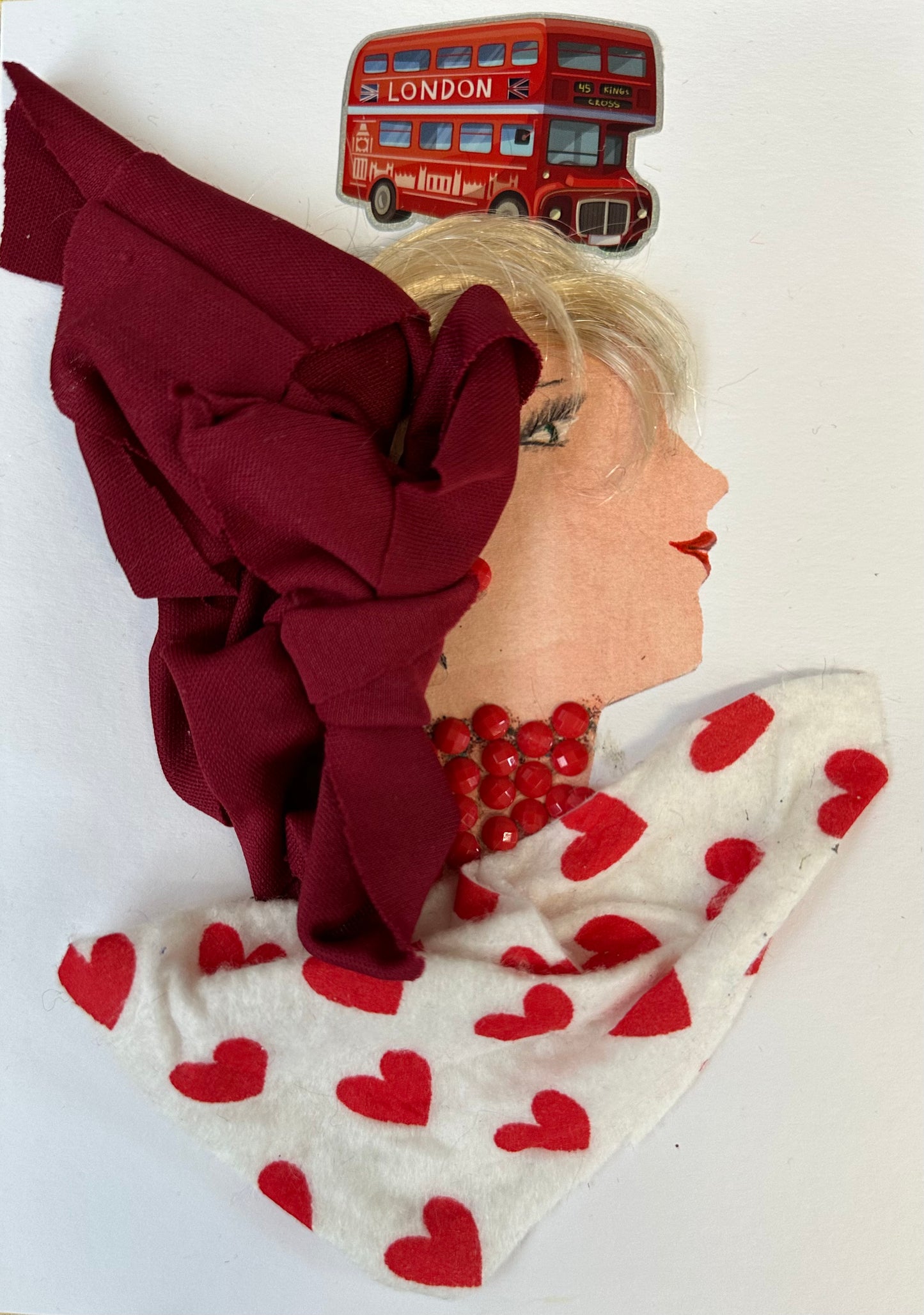 I designed this handmade card of a woman dressed in a white blouse with red hearts. She has a dark red hatinator and a necklace made up of bright red gemstones. Above her head is a double-decker red bus.