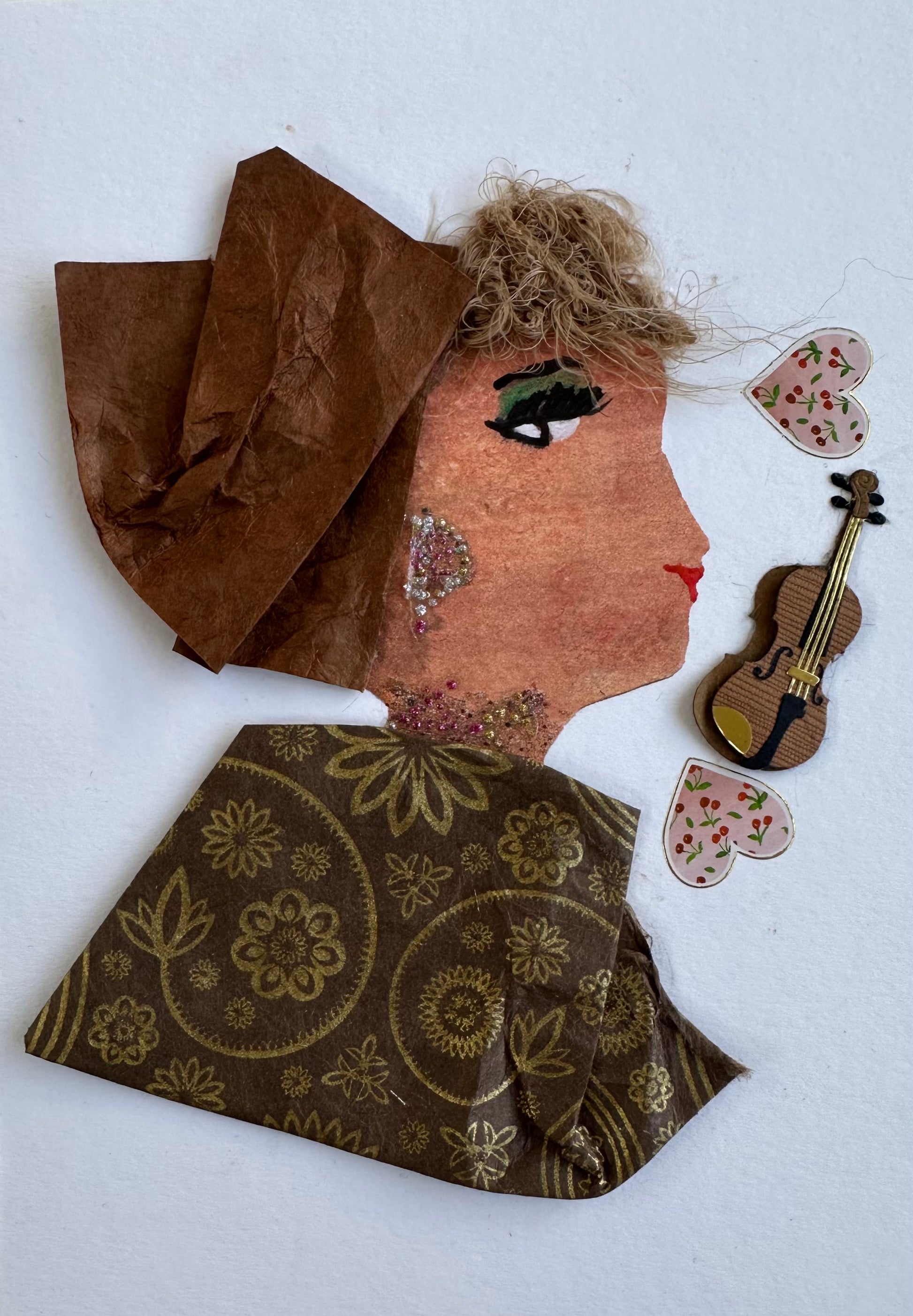I designed this handmade card of a woman dressed in a brown blouse with a gold coloured flowers and designs painted on it. Her hatinator is a lighter brown, and she is wearing pink and silver gemstones jewellery. Next to her face is a violin and two pink hearts with small cherries patterned inside.