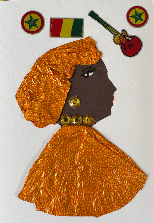 I created this handmade card of Kilburn Kristine. She is dressed in a matching hair wrap and blouse which are orange with small yellow spots. Her earring and necklace are a yellow-gold gemstone. The card is completed with a red, yellow, and green guitar, flag, and stars. 