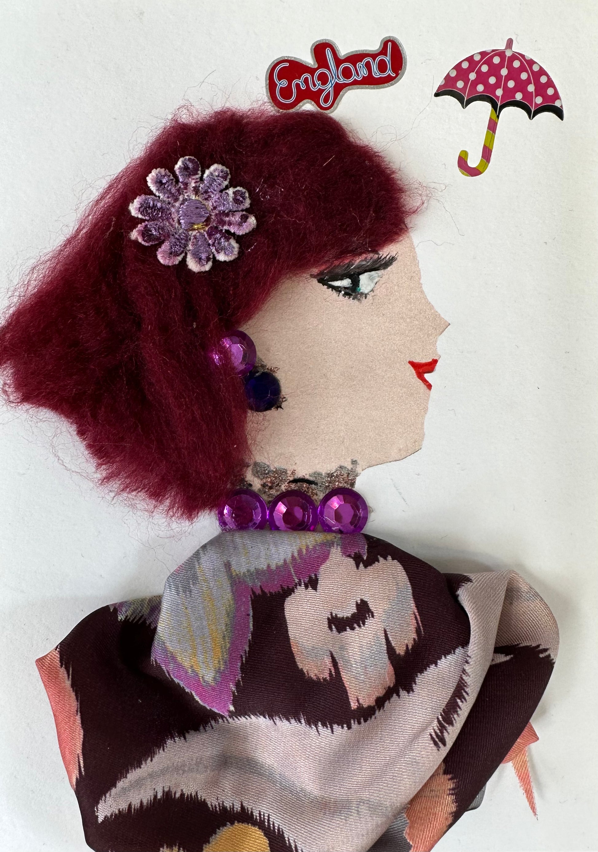 I designed this handmade card of a woman wearing a multi-coloured blouse with a purple flower hair piece She has red hair and an umbrella in the right corner.