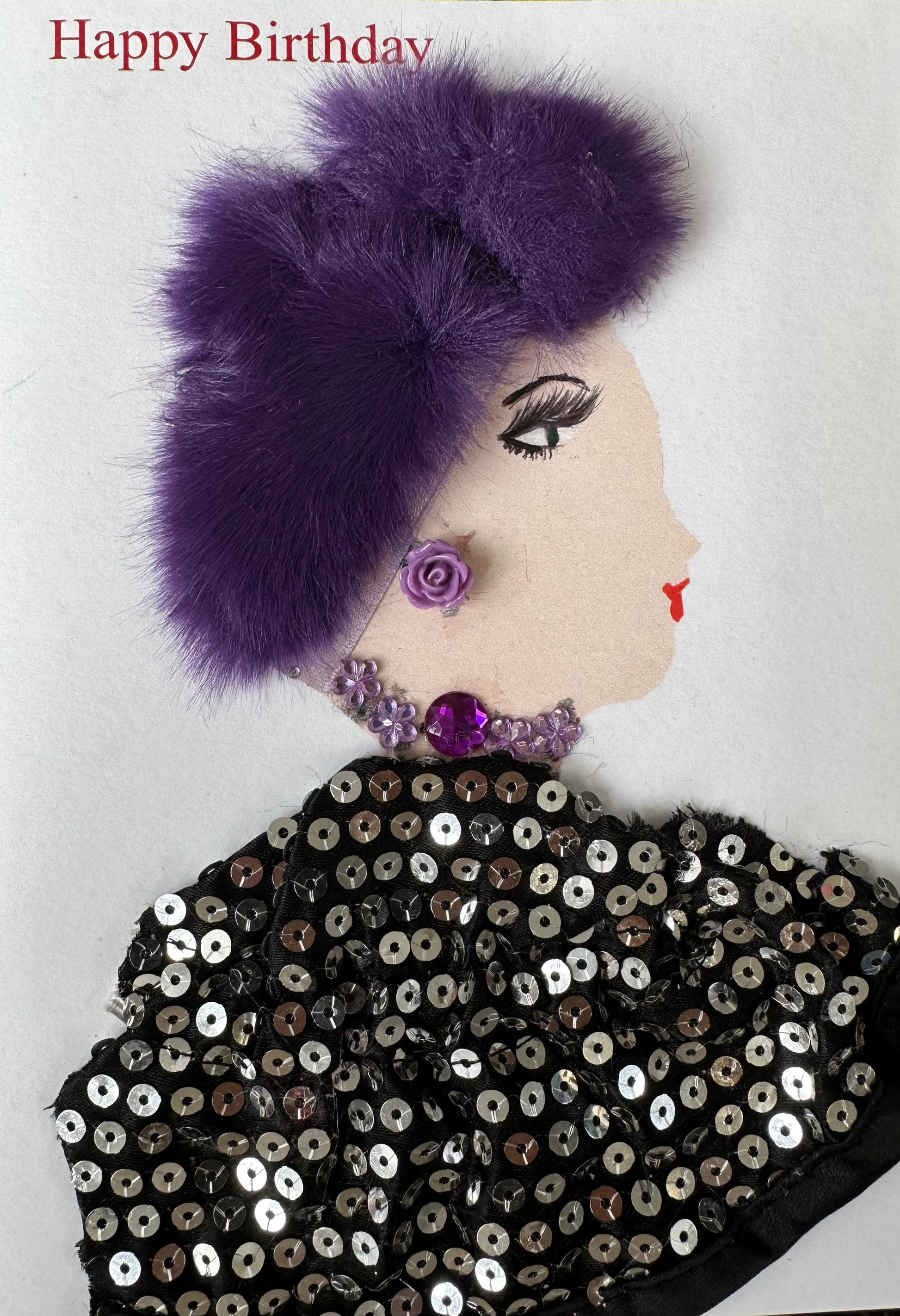 I made this handmade birthday card. The woman, Acton Ashlynn, is dressed in a black blouse with silver sequins. Her hair is a dark purple which matches her purple, flower earrings and necklace. 