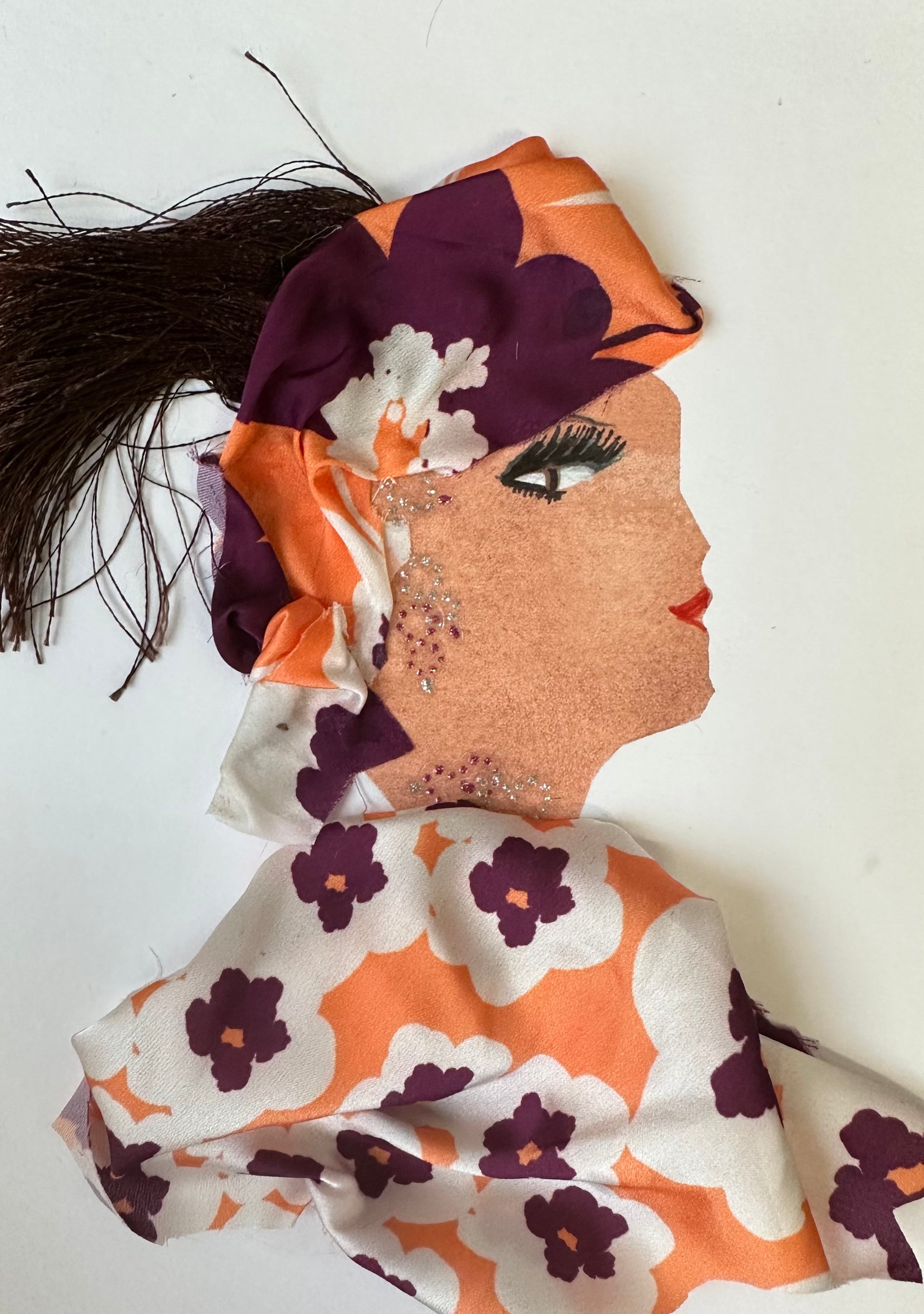 I designed this handmade card of a woman dressed in a purple, orange, and white floral blouse and hatinator. Her hair is held together by the hatinator, and her jewellery is composed of small gemstones.