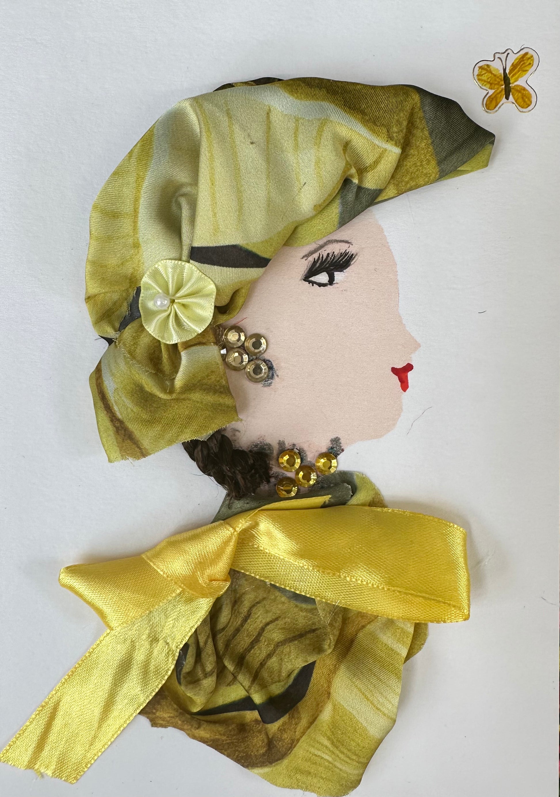 I designed this handmade card of a woman dressed in a multi-yellow toned silk blouse and hatinator. The blouse is completed with a yellow ribbon collar, and her hatinator is pinned back with a flower-shaped clip. To complete her outfit, she has yellow gemstone jewellery and a butterfly flying next to her.