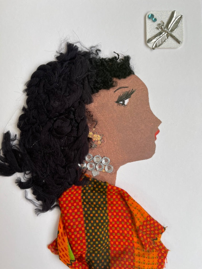 This card is called Dayna. She wears an orange patterned blouse, and has long curly black hair. In the top right corner, there is a sticker of a dragonfly. 