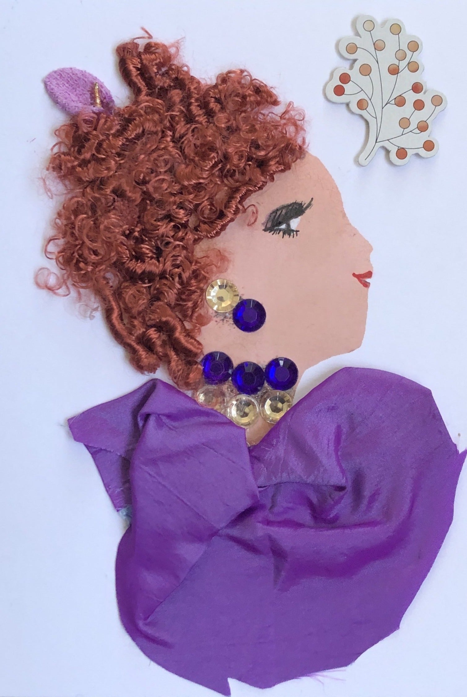This card is called Perivale. She wears a purple silk blouse, and her hair is bright red and curly. Her jewellery is purple and tan coloured gems. In the righthand corner there is a small sticker of a pink plant. 
