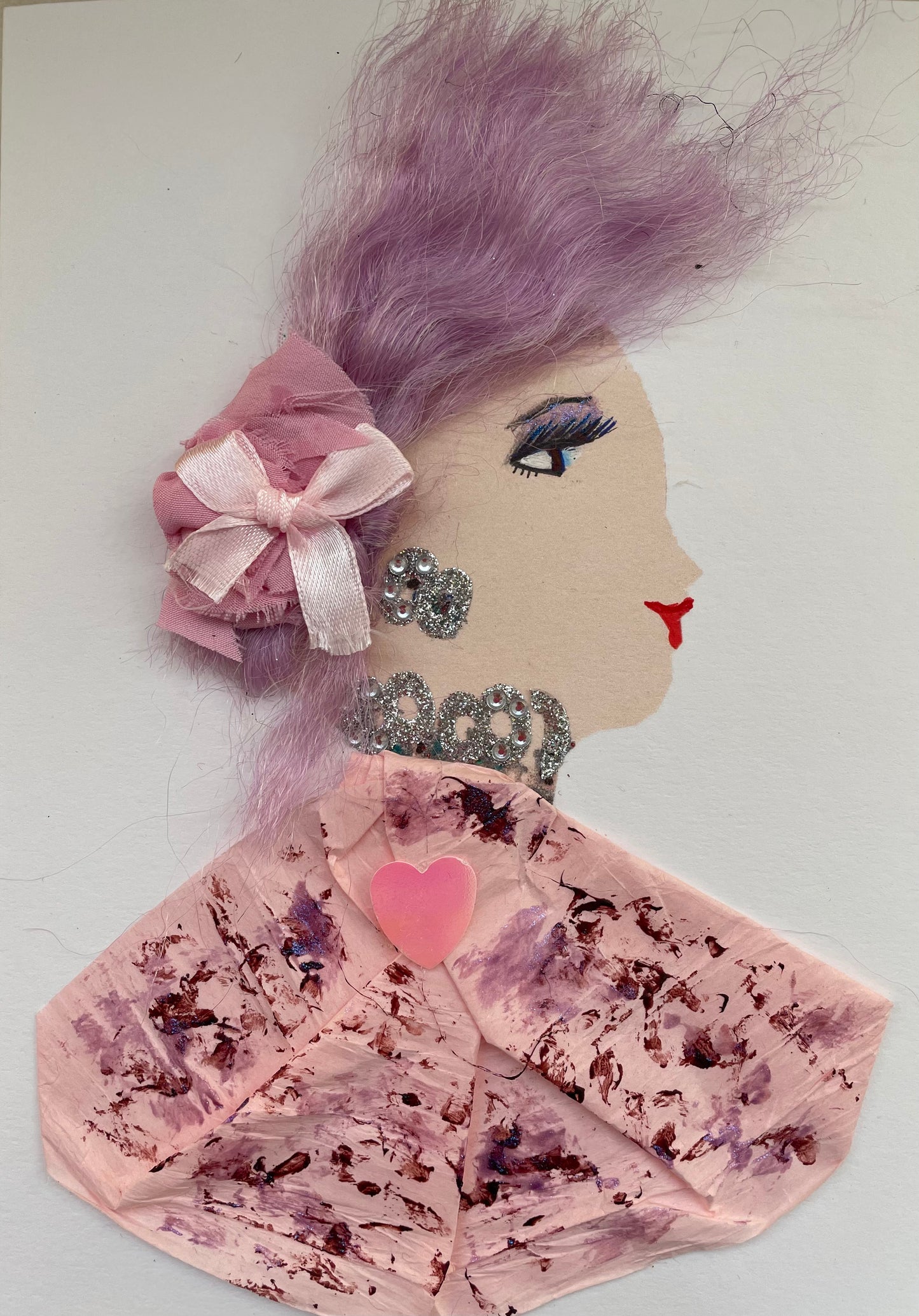 She is wearing a light pink patterned blouse with splashes of purple paired with a matching diamanté necklace and earrings. On her  blouse, there is a hot pink heart jewel attached. She also has gentle lavender coloured hair accompanied by a light pink bow used as an accessory. A beautiful card  to frame for your home or the perfect gift for someone to celebrate. 