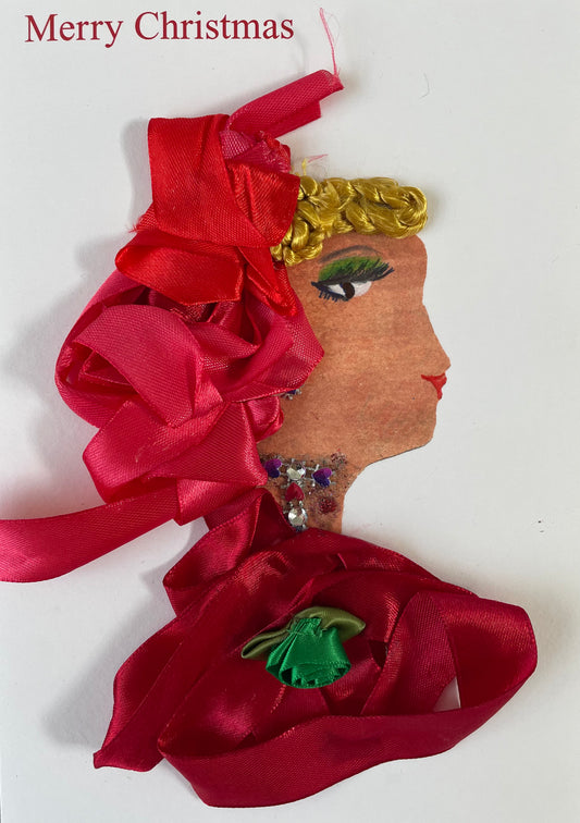 I have called this card Penelope Peninsula. She is wearing a dark red blouse with a green accessory in the middle. She is wearing a red headpiece complimenting her blonde hair. She has a yellow, red and purple diamanté necklace.