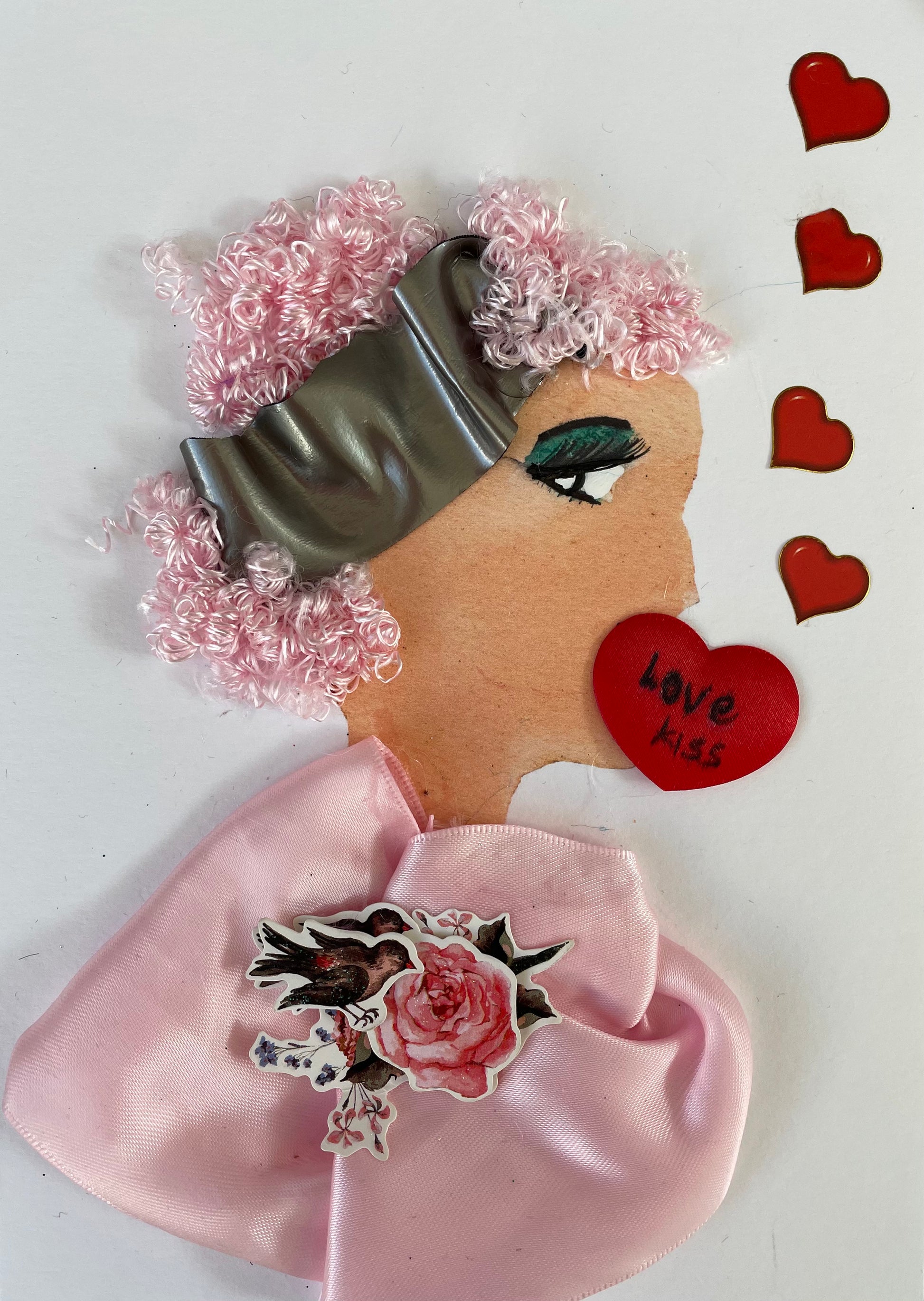 This ​ a ​is unique card which can be framed as a gift or used as a traditional greeting card. Useful for a birthday or keepsake .I made this card to show  a woman wearing a pink blouse and has pink curly hair with a grey hair band. She has her lips covered with a heart and love kiss written on the heart. There are 5 red hearts on the picture that come from the side​ reflecting love.​ ​There is a  paper pendant in the middle of her blouse ​showing​ brown birds perching , on ​a ​pink rose 