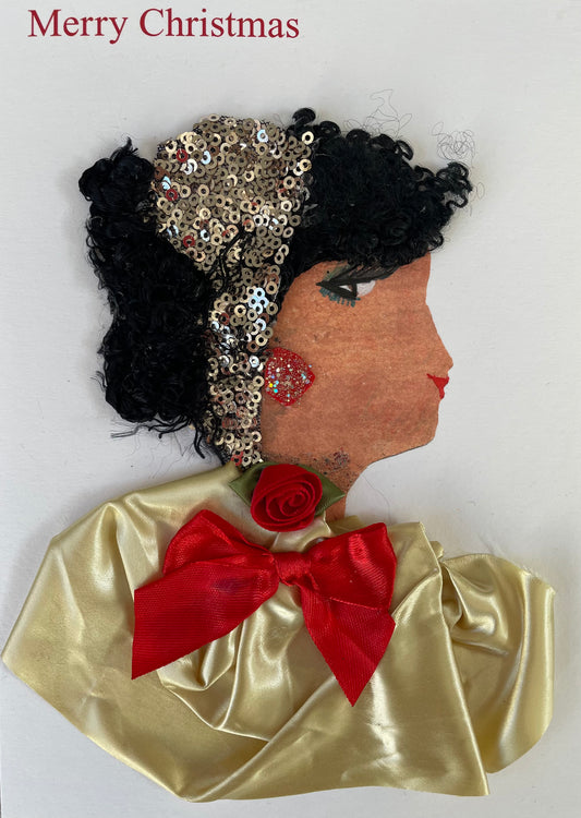 andmade Christmas card showing the side profile of a woman with curly black hair, decorated with a section of gold sequins. She has red lips, green eyeshadow, and a glittery red earring. Her outfit is made from shiny pale gold fabric and is adorned with a red ribbon bow and a small red fabric rose at the neckline. The background is plain white with the words "Merry Christmas" printed in red at the top left.