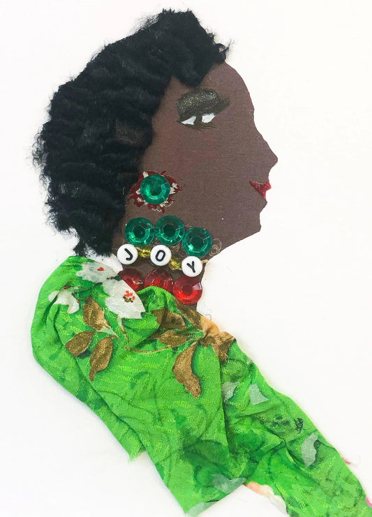 This card has been given the name Jubilee Joy. she wears a green nature patterned blouse. She has three different necklaces, one red gems, one green gems, and one that says joy in beading. She has short black hair, and her green earring is peeking out. 