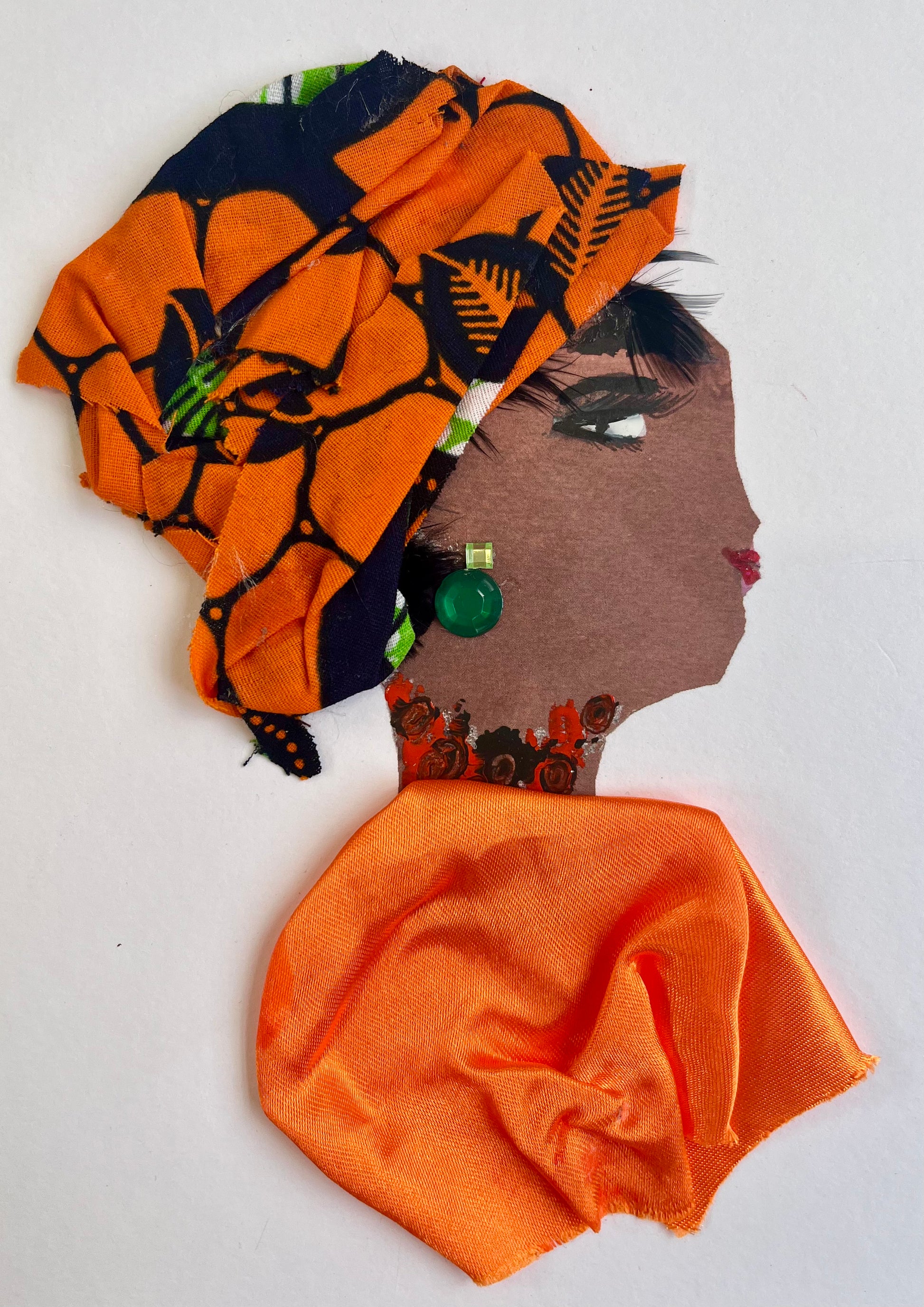 This card is called Kehlani. She wears a bright orange blouse and a headscarf which has orange and black in it. Her earring is a green gemstone. 