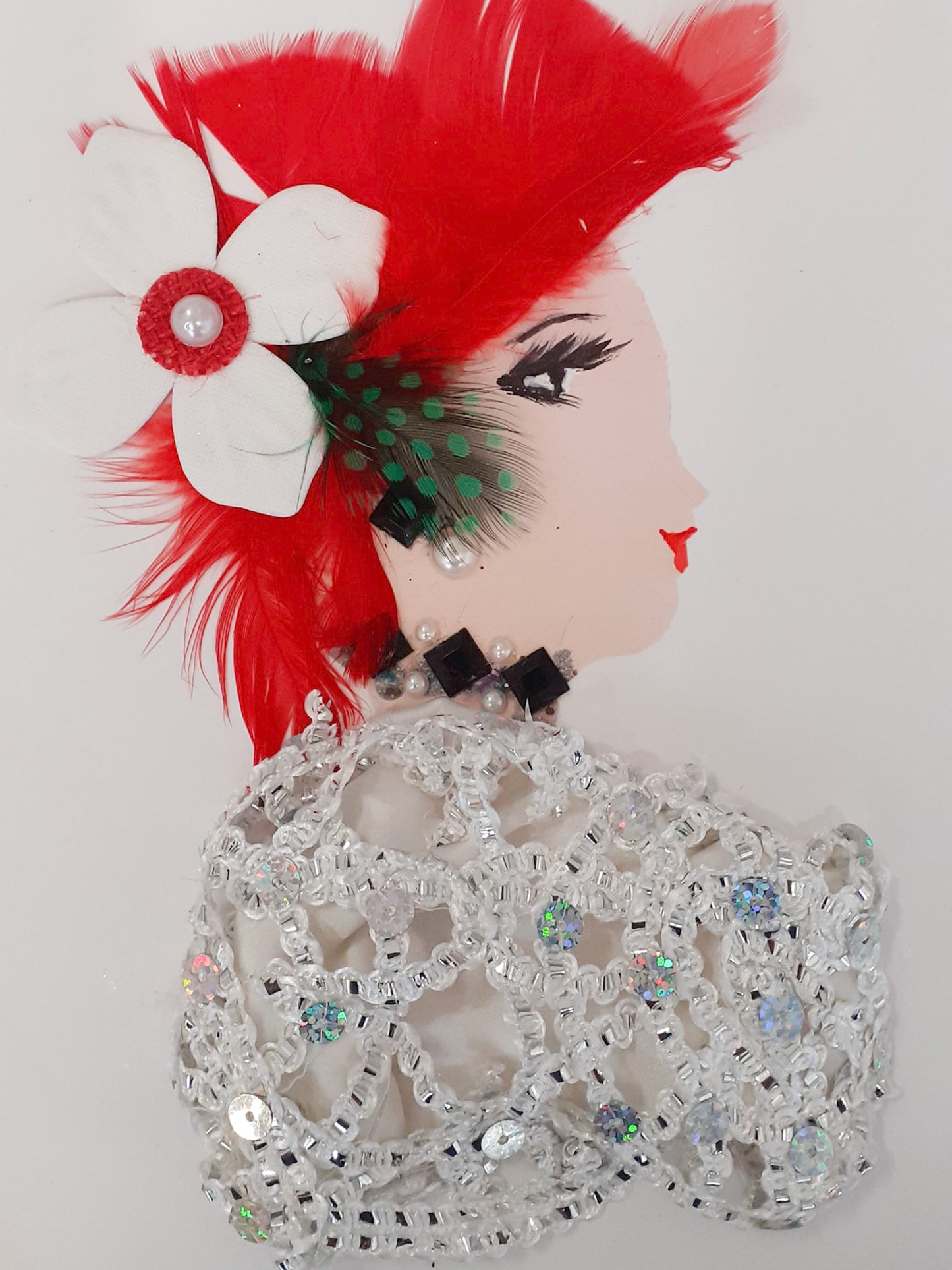 This card is named Dazzling Dazie. She is wearing a white dress made of a white and silver sequined material, a black diamond necklace, and on her head there is a red feather headress with another black and green polka-dotted accent feather. 