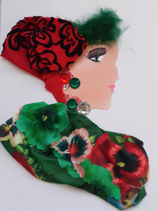 This card is given the name Claudia Cloverleaf. Claudia wears a floral print fabric with green and red flowers, and a red headdress to cover her green hair which has black embroidery on it. 