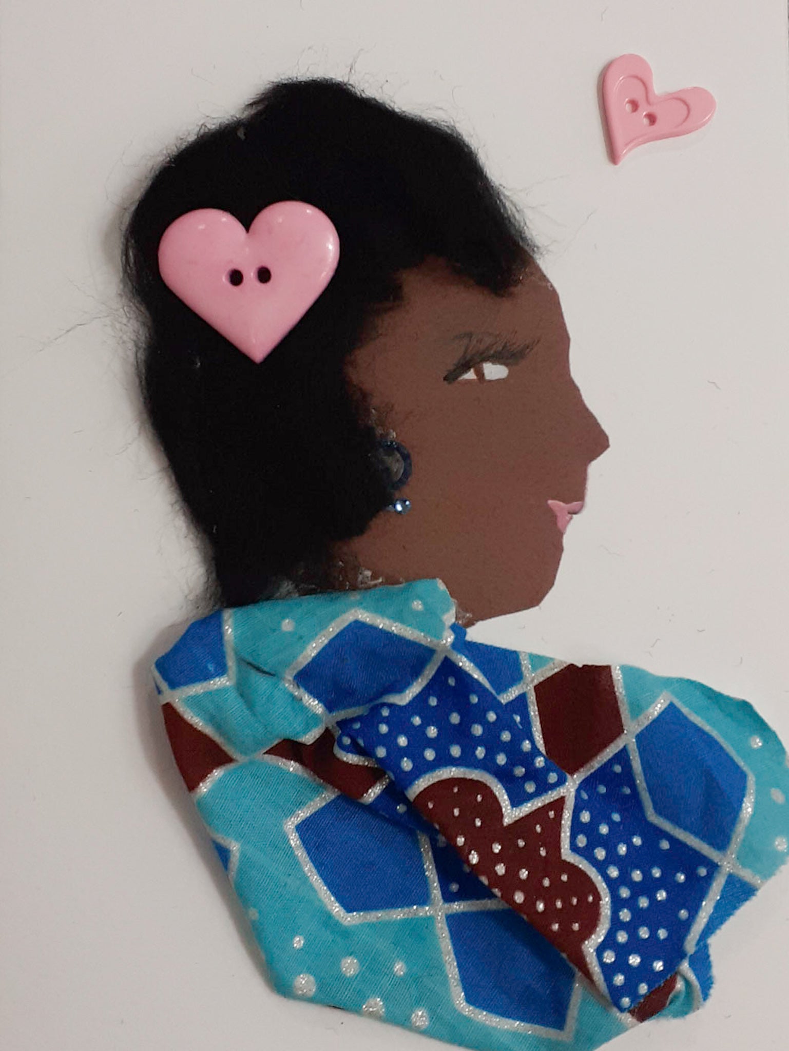 This card is of a woman named Natasha. Natasha wears a light blue, medium blue, and deep red patterned blouse with silver glitter lines throughout. In her short black hair, there is a light pink heart-shaped button. On the top right corner, there is a small pink heart. 