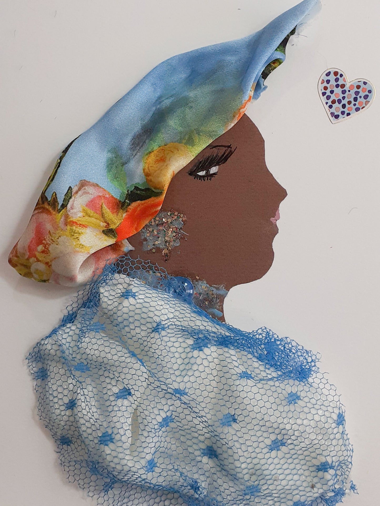 This card has been given the name Bethnal Green Princess. Bethnal wears a white blouse which has a light blue netted overlay, and a floral patterned silk scarf around her head. Her jewellery is made up of blue and gold glitter. 