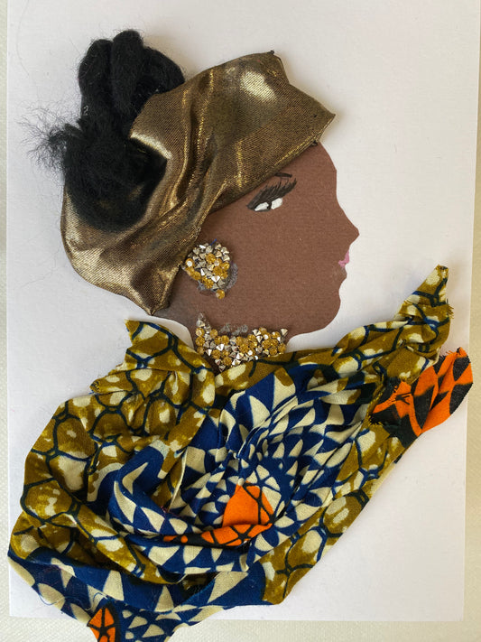 This is a handmade card of a woman named Maybelline Merry. Her hair is styled in soft black fibres, partially wrapped with a shiny gold fabric. She wears sparkling gold gem earrings and a matching necklace. Her outfit is made from patterned fabric in deep blue, olive green, and bright orange, arranged in elegant folds.