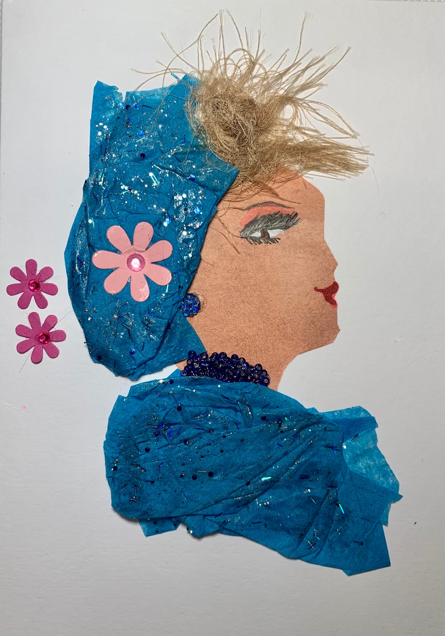 This card shows a woman wearing a blue matching dress and headscarf which has blue glitter on it. On the headscarf, there is a pink flower. In the background, there are two more pink flowers. 