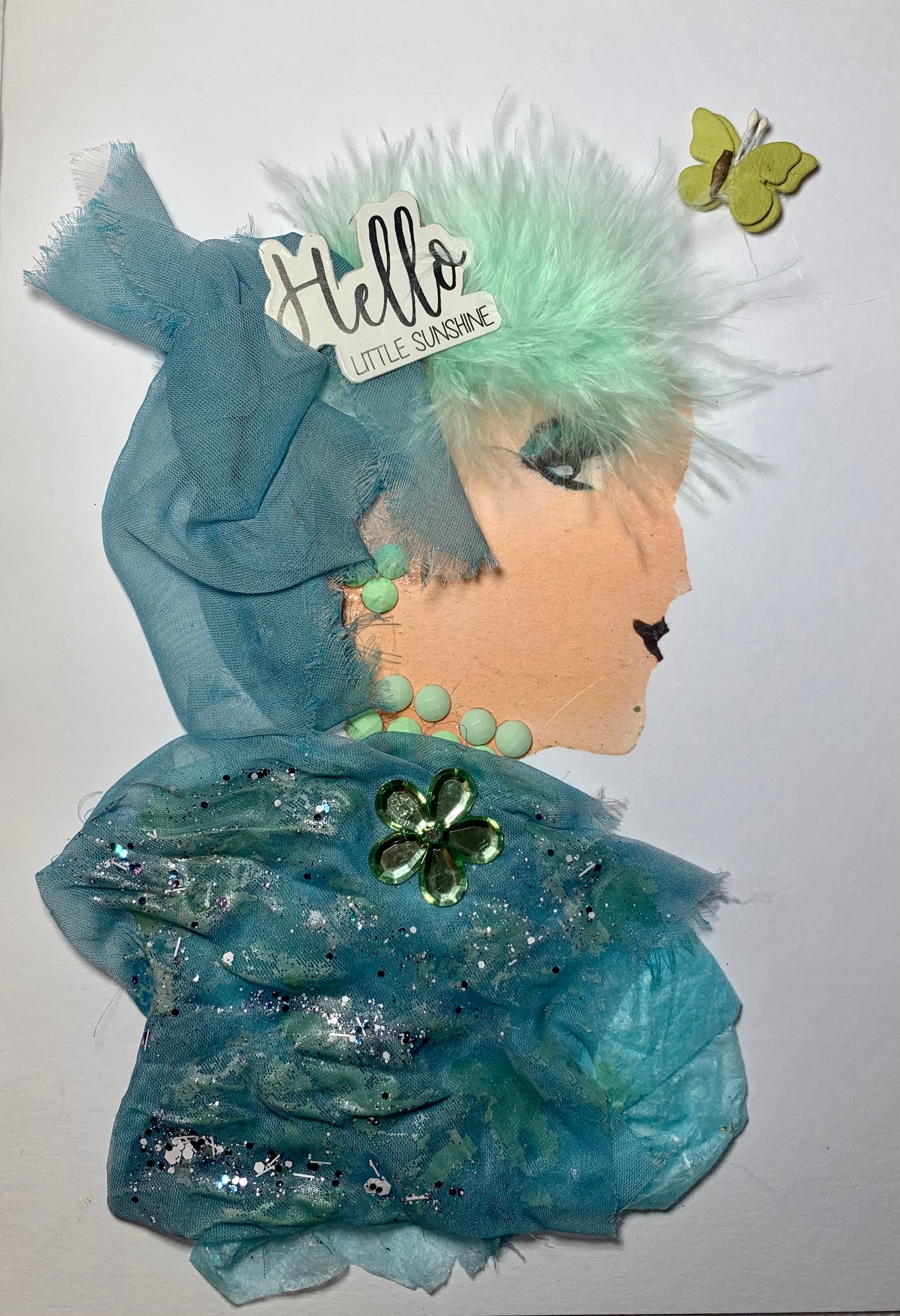 This card shows a woman wearing a blue blouse and headscarf which is dazzling with sparkles. She has a quote nestled into her green feathery hair that says "Hello Little Sunshine" and there is a lime green butterfly on the top right hand side. Her jewellery is also lime green.  A great card  to cheer yourself or someone up .