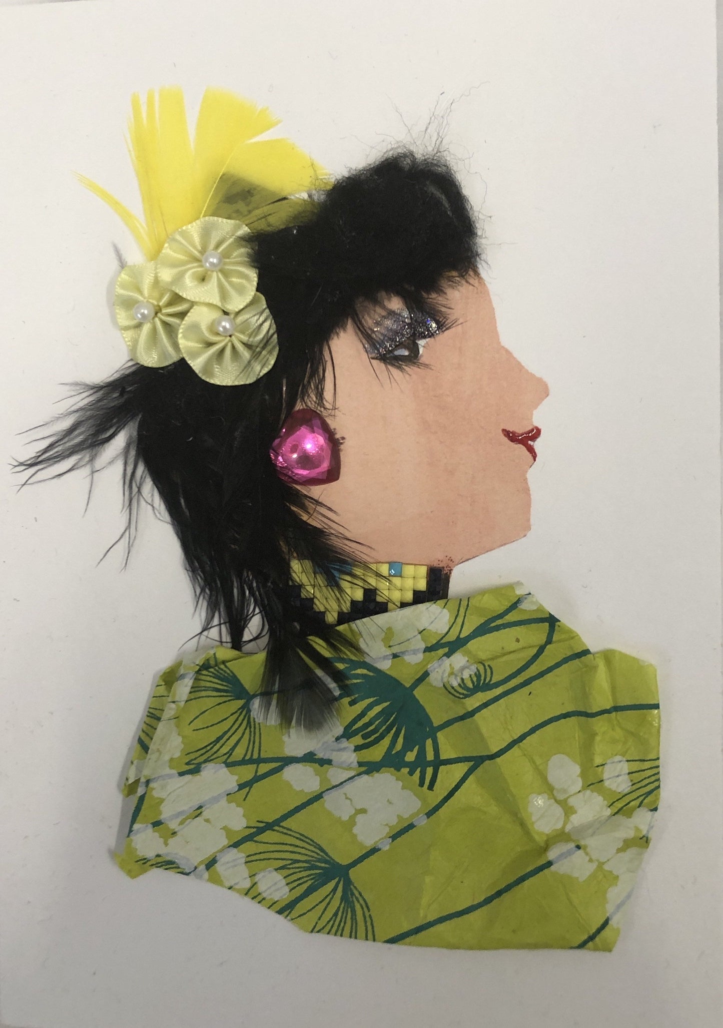 This card has been given the name Chelsea Chick. Chelsea wears a green blouse with a cherry blossom pattern on it. In her black hair she wears a yellow flower with a yellow feather behind it, and a pink heart gem earring. 