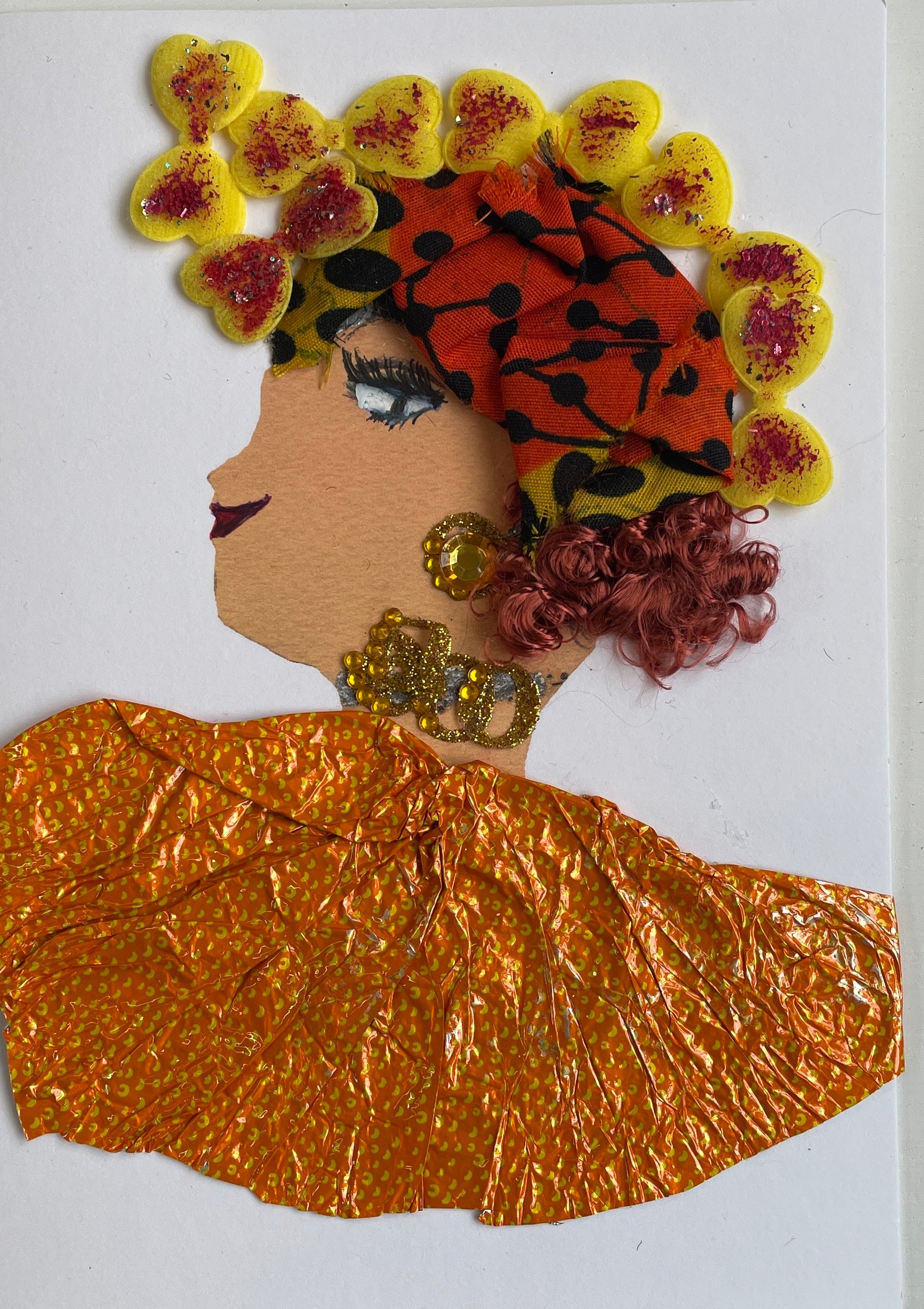 This image shows a woman called Brigadier. She wears a dress made of a metal material that is orange with small yellow designs on it. Her necklace and earrings are both a combination of silver and gold. Her deep red hair peeks out the bottom of her headscarf which is orange and yellow with a black pattern on it. There are small yellow bows around the headscarf, each covered with red glitter.