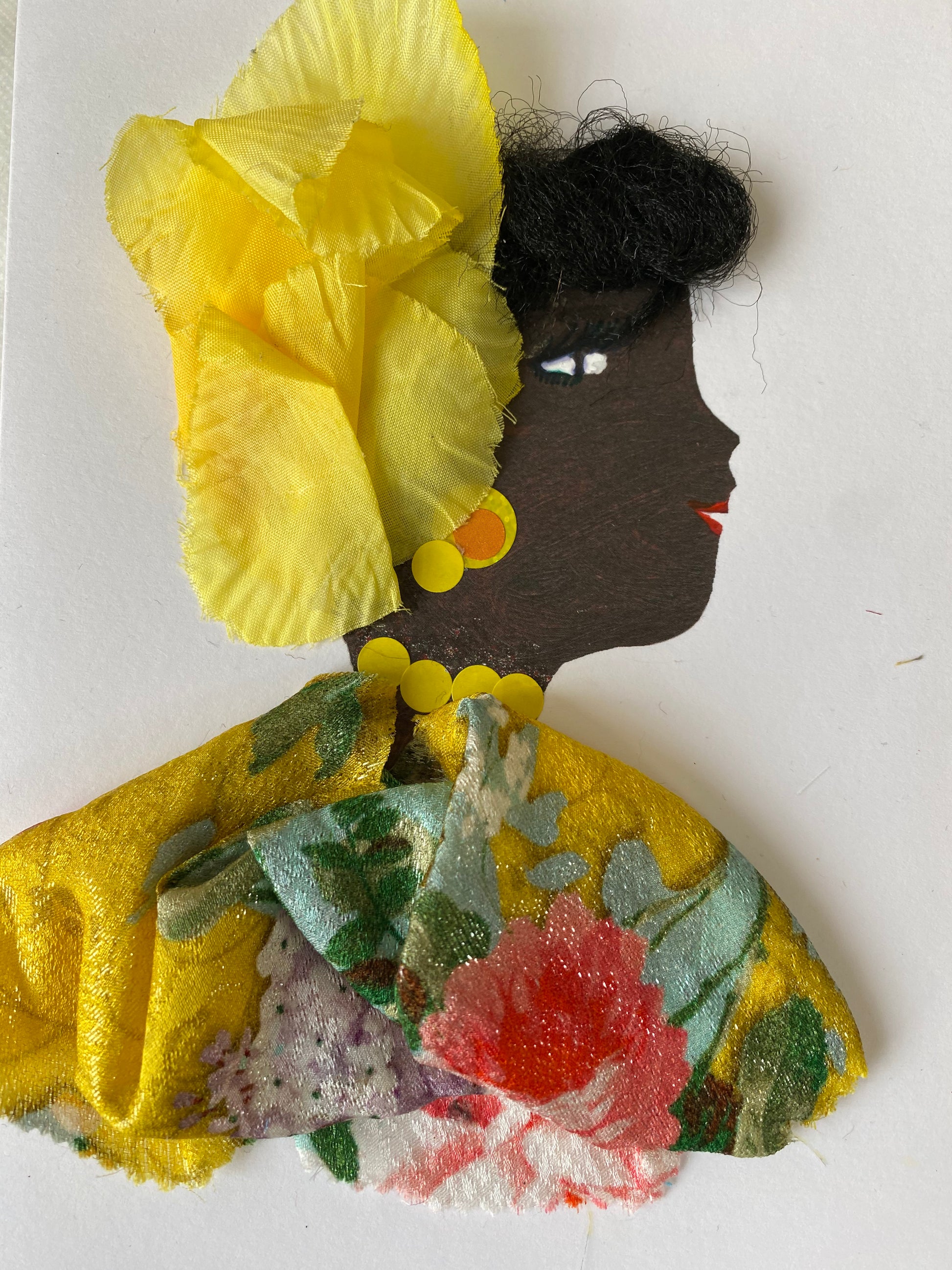 I designed this card of a woman named Delilah Diligent. She has a black skin tone and is wearing a charming yellow hat. She wears a yellow floral blouse. She wears stunning yellow jewellery.