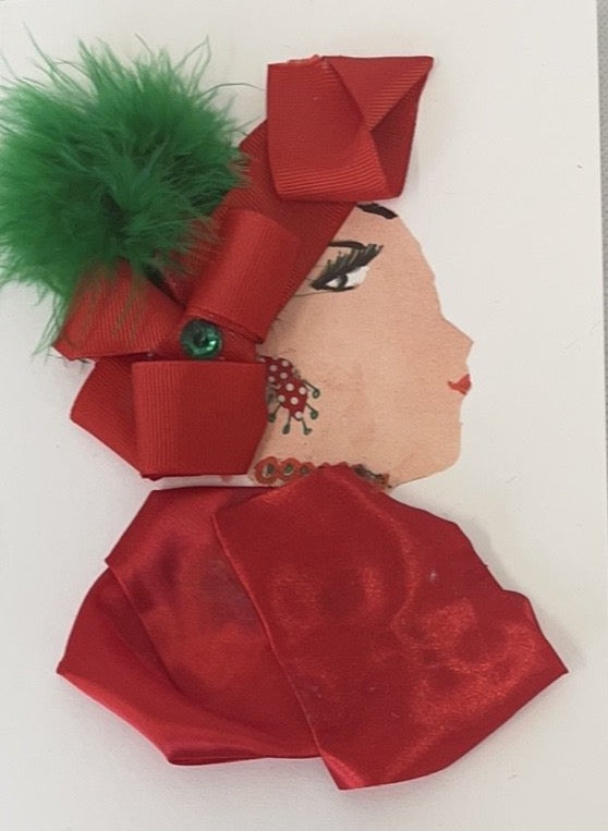 This card has been given the name Christmas Mum. She wears a red satin blouse with a matching ribbon in her hair. There is a green pom pom on top of the ribbons.