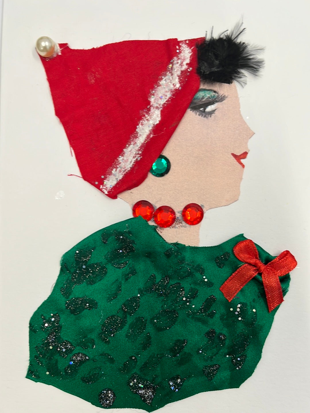 This card is called Christmas Elf. She wears a sparkly green blouse with a red bow, and a red santa hat. 