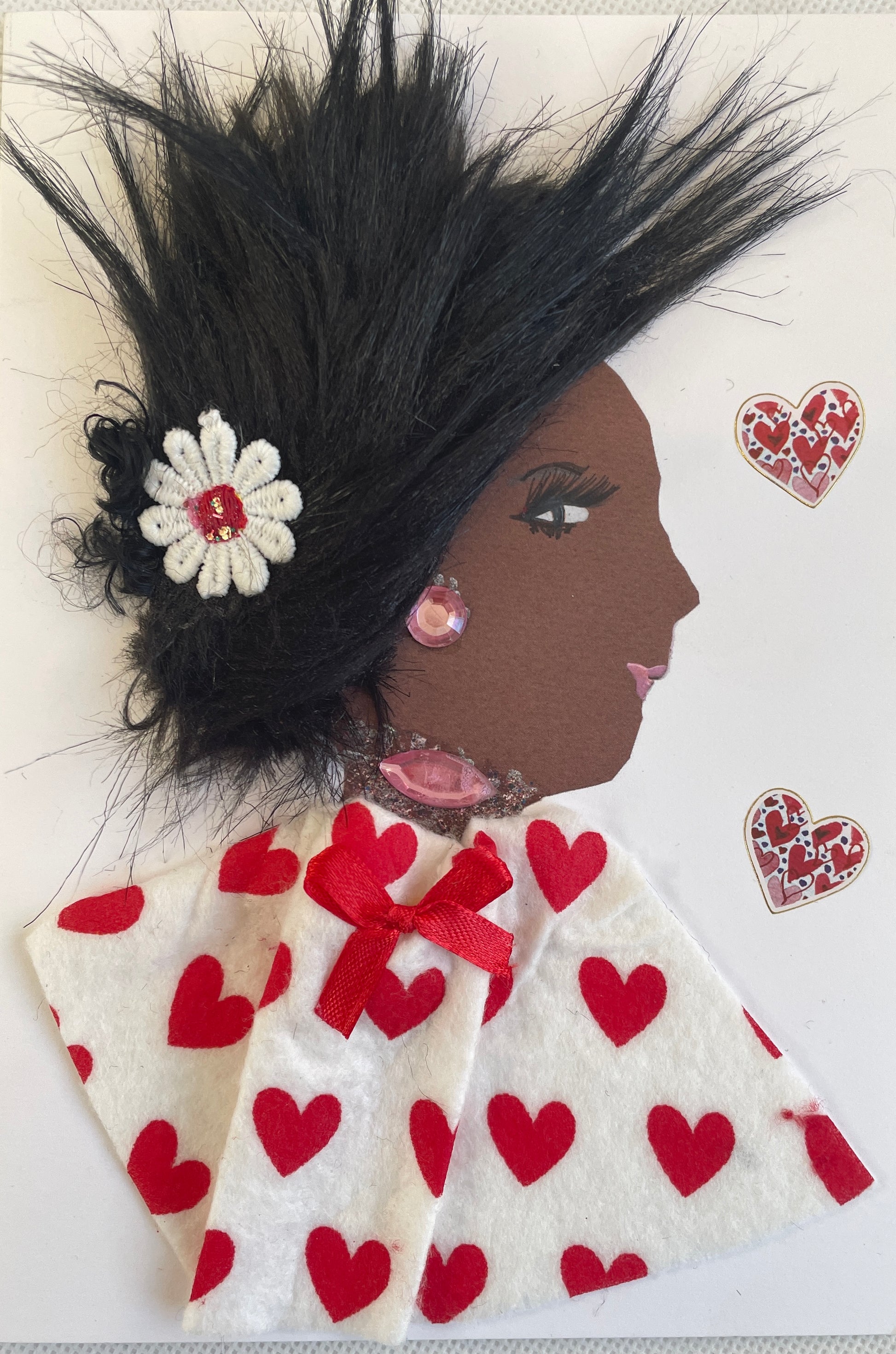 This  picture has a black  woman I have called Elizabeth wearing  a blouse decorated with red hearts and a matching red bow. There is a single flower in her spiky hair. She has precious pink jewellery on as well. There are two red hearts on her right side. 