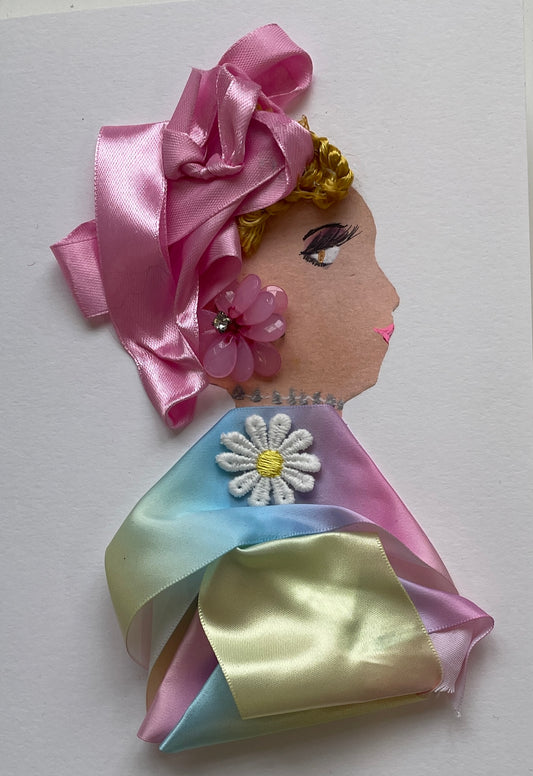 This card is called Doctor Colourful. She wears a ribbon as a blouse which is rainbow, and a white daisy on the front. She wears pink ribbons in her short blonde hair, and a flower gem as her earring. 