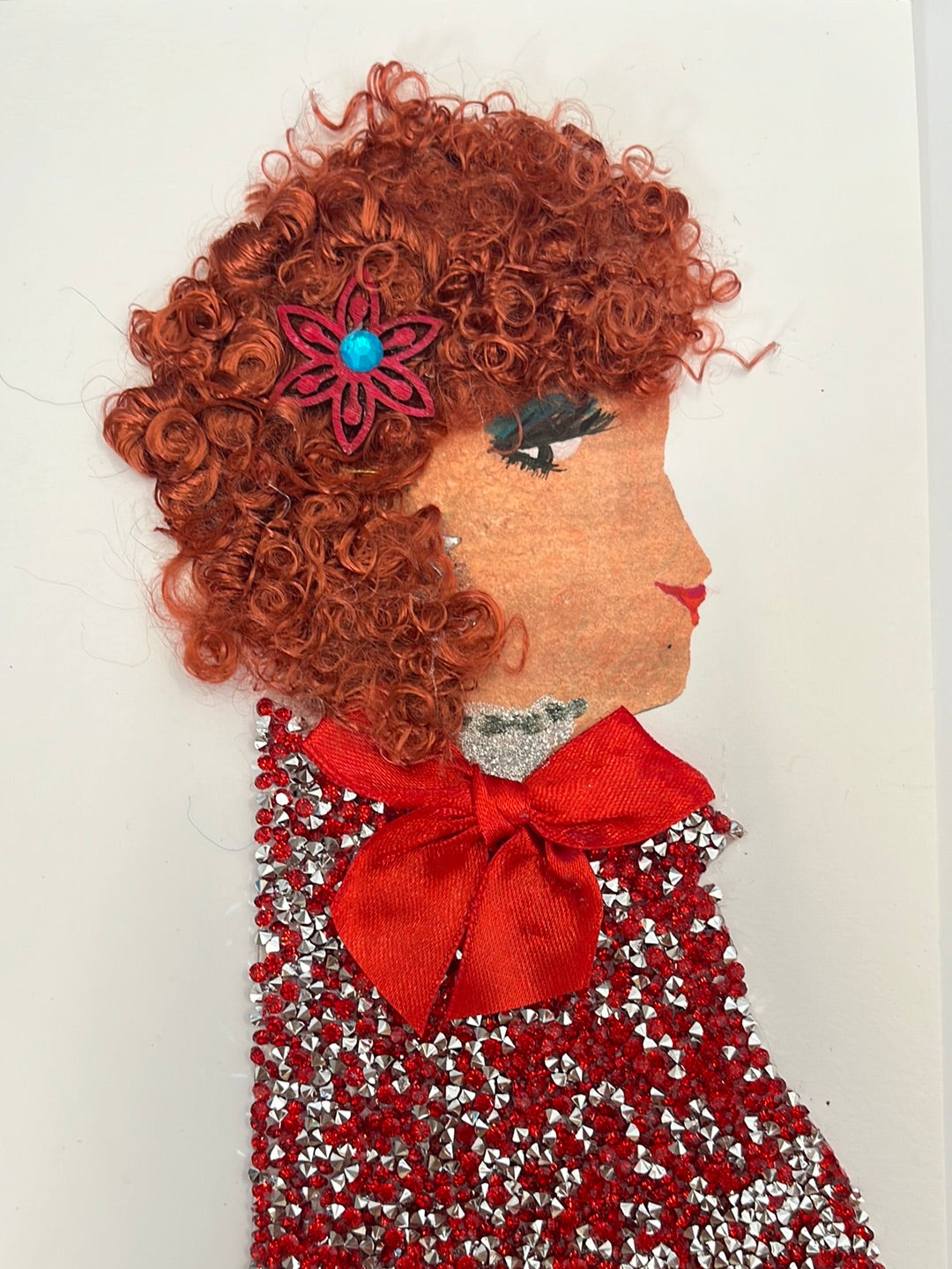 She wears a diamond red sparkly top with a large red bow on it. Her hair is red and curly.She has a flower in it. 
