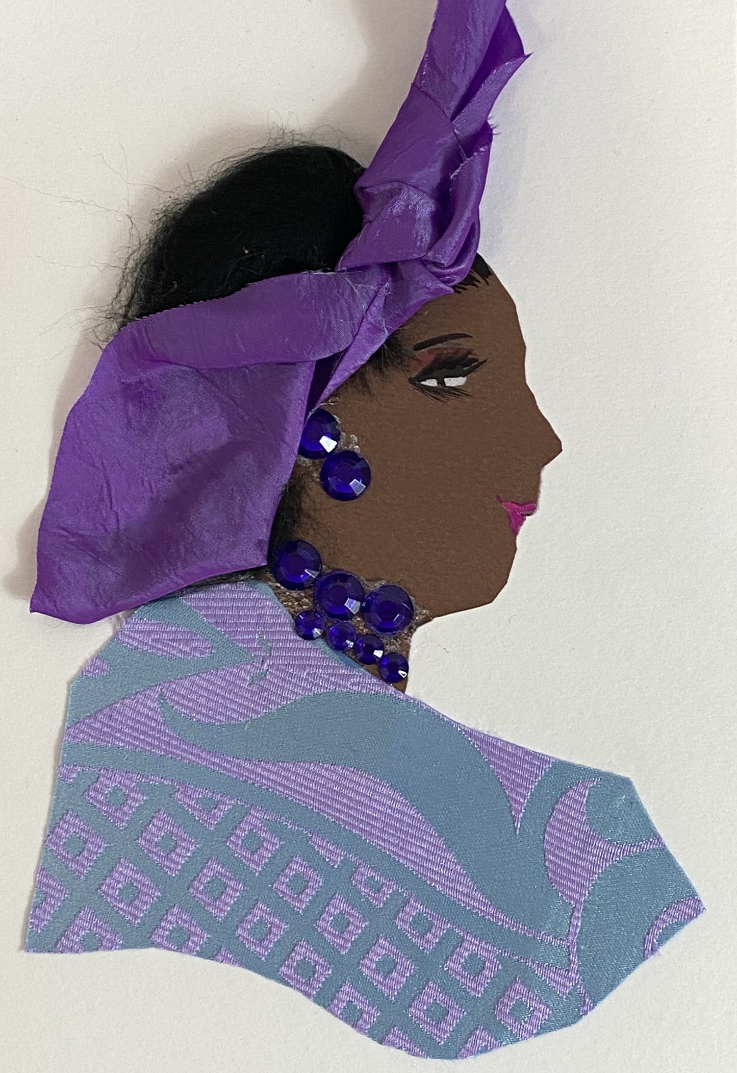 This card is called Peju. She wears a patterned blouse which is light blue and lavender, and a purple headscarf in her black hair. 