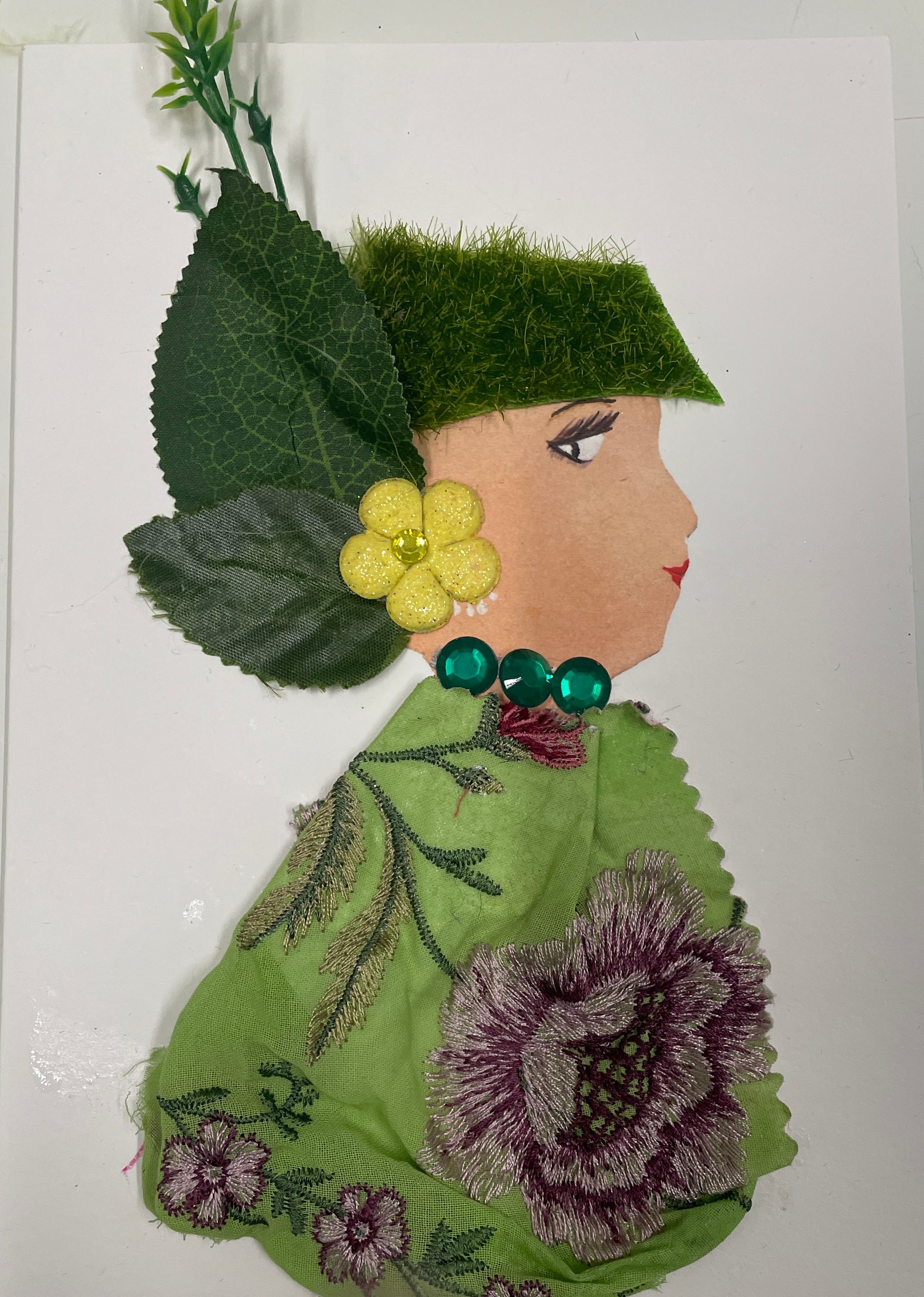 I designed this card of a woman named Super Garden. She has a white skin tone and wears a green grassy type covering for her hair.  cover, yellow flower earrings with a leaf extension, an emerald green necklace and a patterned blouse.