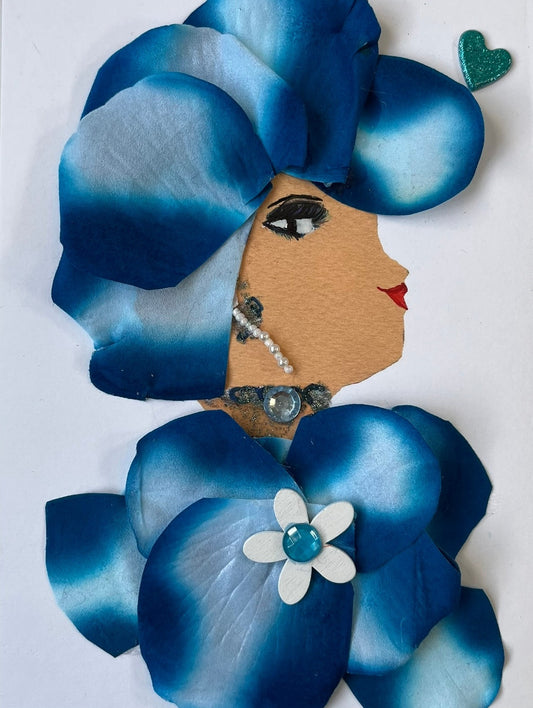 This card has been given the name Dr. Dasani Dagenham. She wears a matching dress and headdress, both made up of blue flower petals which have a gradient to white in the middle of each petal. She wears a flower pendant on her dress which is a white daisy with a blue gem in the middle. Her necklace is a blue gem which matches the flower. She wears an earring which is are a  tiny string of pearls.