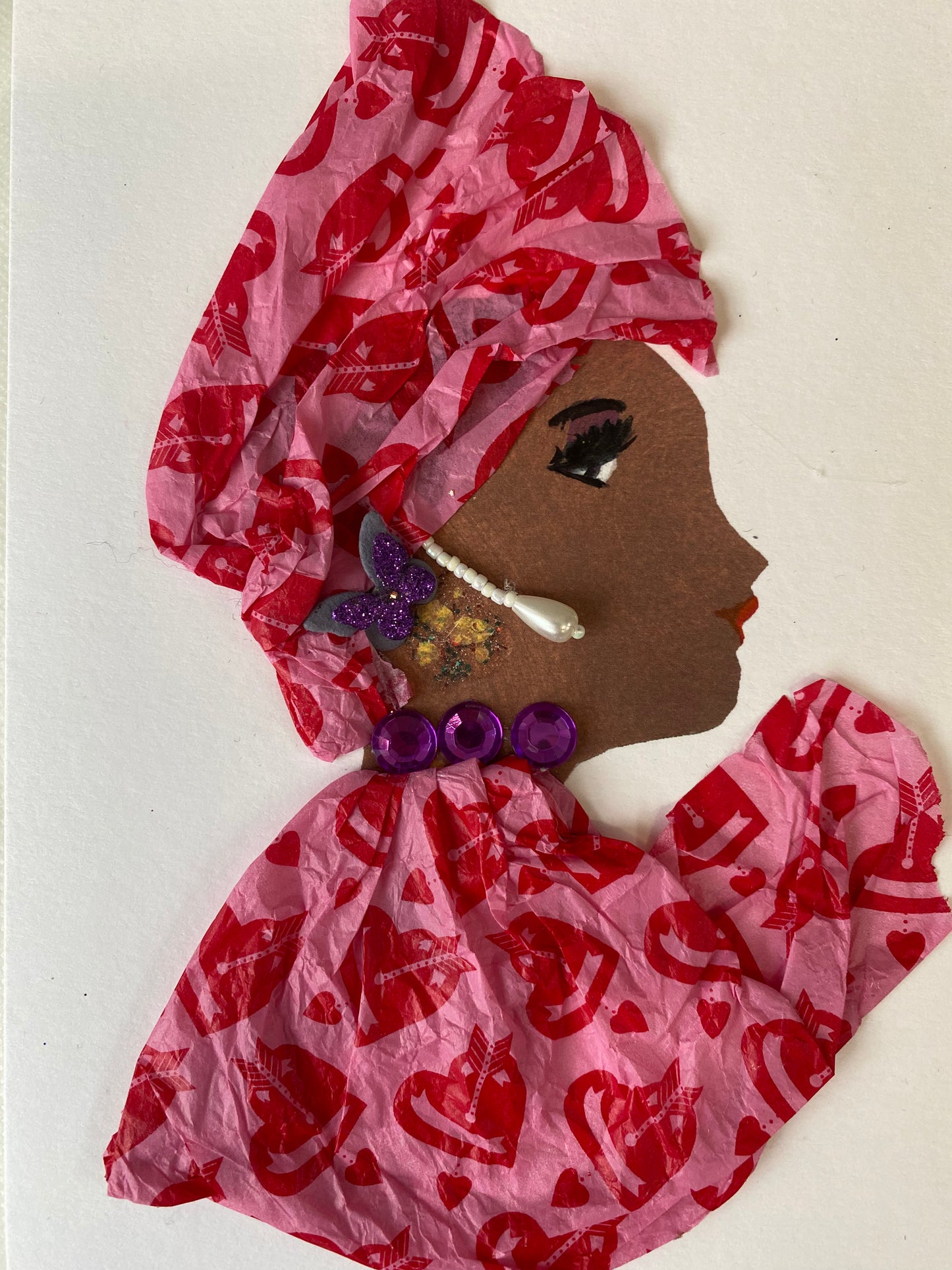 I designed this card of a woman named Raspberry Pink. She has a brown skin tone and wears a pink with red hearts pattern headwrap. She wears a matching pink blouse with a red heart pattern. She wears a purple necklace with dangling pearl earrings. To the side of her earring there is a sparkly purple and gray butterfly. 
