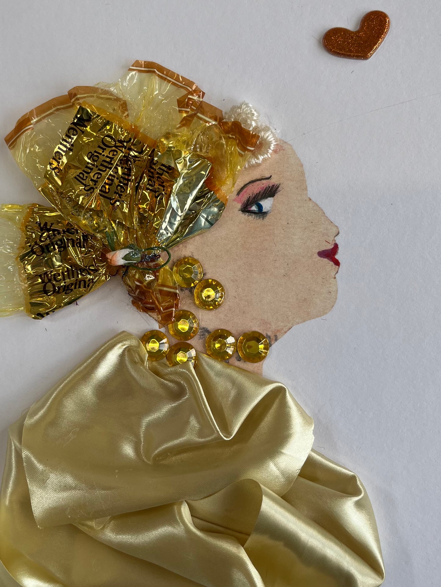 A card depicting a woman dressed in gold made from sweet wrappers with silky fabric  and sequins. She has sweet wrapper hat to reflect her beauty and style..
